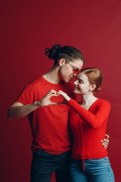 Valentinspaar Porträt einer lächelnden und umarmenden jungen Schönheit und ihres gutaussehenden Freundesmannes, der an ihren Händen Valentinstag in Form eines Herzzeichens macht