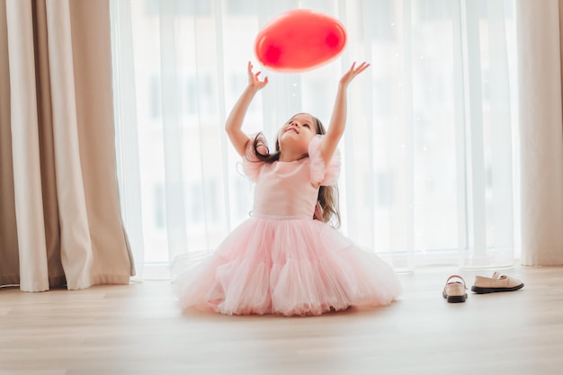 Valentinstag Baby Ein kleines Mädchen in einem roten Kleid hält einen großen Ball in Form eines Herzens