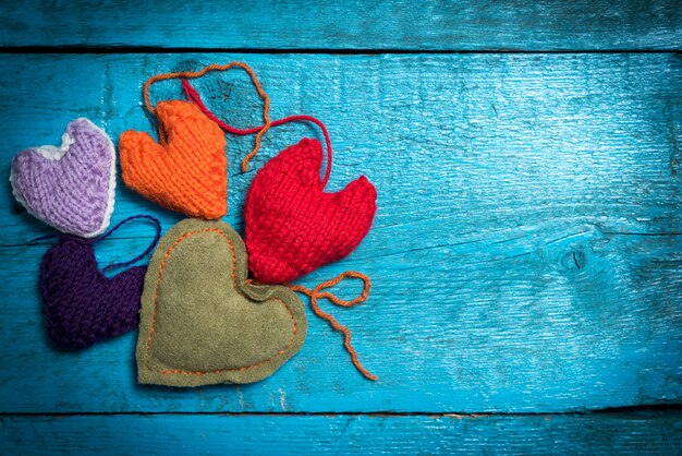 Valentinstag. Bunte gestrickte Herzen. Rotes Herz auf den blauen Brettern. Valentinstag. Herzanhänger. Rotes Herz. Valentinskarten.