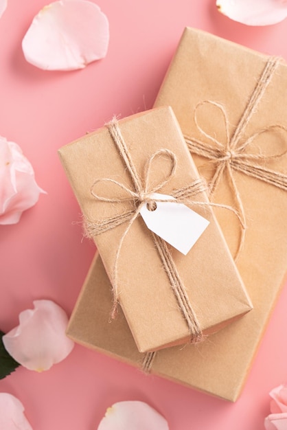 Valentinstag-Design-Konzept-Hintergrund mit rosafarbener Rosenblume und eingewickelter Kraft-Geschenkbox auf rosafarbenem Tischhintergrund