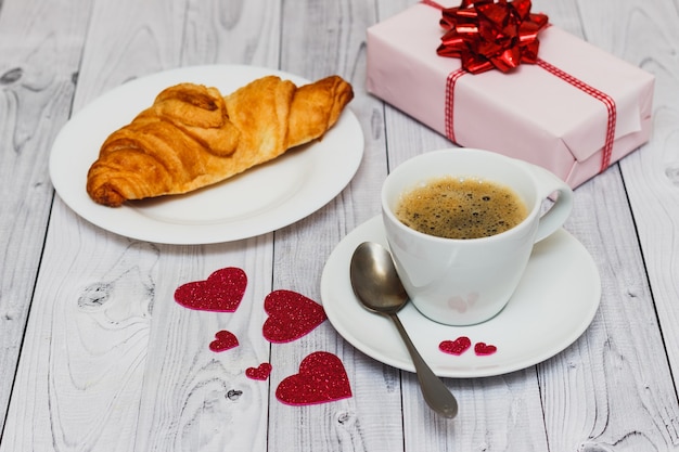 Valentinstag Frühstück mit Kaffeetasse, Croissant und rosa Geschenk