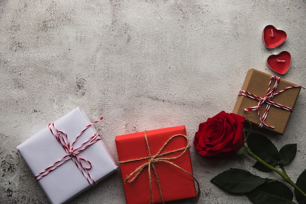 Valentinstag, Geschenkbox aus Kraftpapier mit einem Band, Rose und Kerzen auf grauem Hintergrund