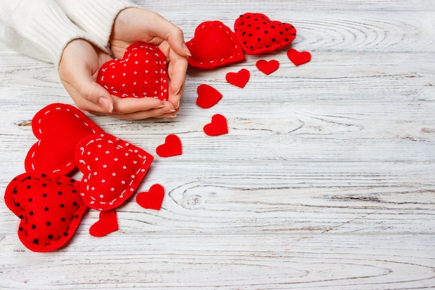 Valentinstag-Grußkarte. Handgemachte Herzen auf Holztisch. Mädchen hält ein rotes Herz. Draufsicht mit Kopienraum