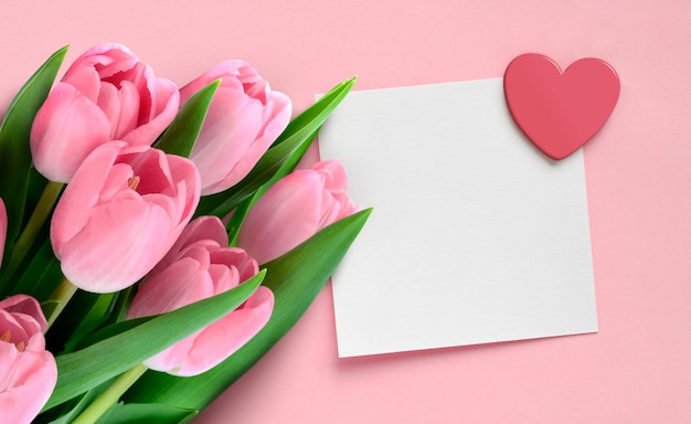 Valentinstag-Grußkarte mit rosa Tulpen und leeres Papier mit Herz auf rosa Hintergrund.