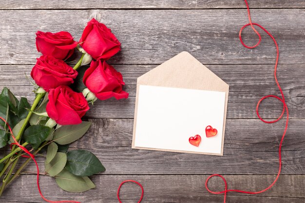 Valentinstag-Grußkarte mit rotem Rosenblumenstrauß auf einem Jahrgang auf grauem Holztisch