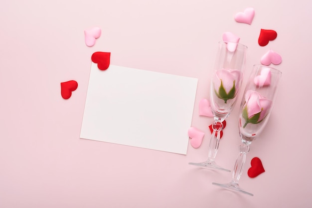 Valentinstag-Grußkarte mit Sektflasche, Geschenkbox, rotem Band und Umschlag mit leerem Notenmodell im Inneren auf rosa Hintergrund. Draufsicht mit Platz für Grüße. Grußkarte mit Kopienraum