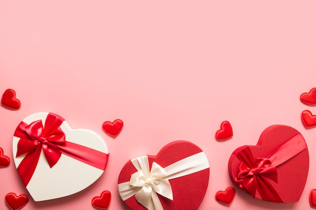 Valentinstag Grußkarte. Rand der roten Geschenkboxen herzförmig und viele kleine Herzen auf rosa. Sicht von oben.