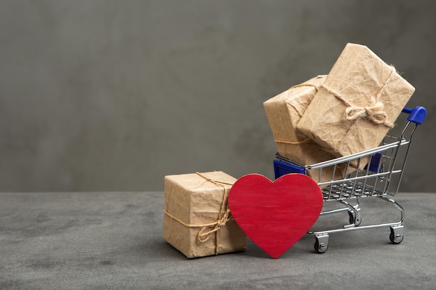 Valentinstag-Grußkonzept Geschenkboxen in einem Einkaufswagen und rote herzförmige Karte mit leerem Platz für Ihren Text Valentinstag-Grußkarte