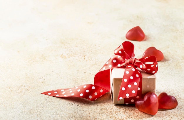 Valentinstag Hintergrund Geschenk in Kraftkarton mit roter Schleife auf rotem Hintergrund mit Herzen Konzept der Hochzeiten zum Valentinstag Neujahr Weihnachten Kopie Raum