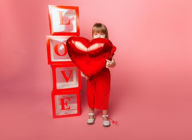 Valentinstag, kleines Mädchen, das einen großen Ballon in Form eines Herzens auf rosafarbenem Hintergrund hält.