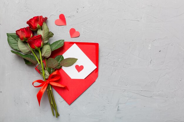 Valentinstag Komposition mit Umschlag Rose Blume und rotes Herz auf dem Tisch Draufsicht flach legen Urlaubskonzept