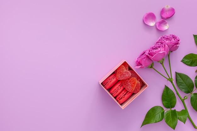 Valentinstag Konzept. Rosa Schachtel mit Marmelade und Makronen und einer schönen Rose auf einem rosa Tisch