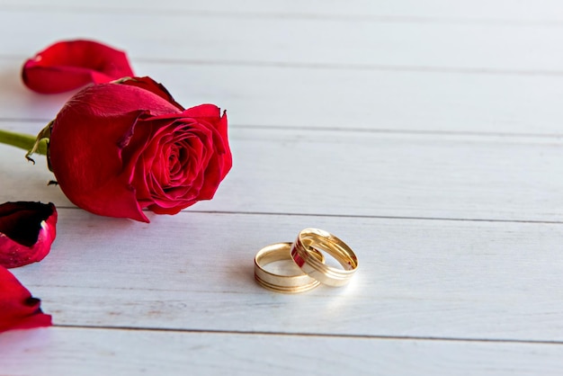 Valentinstag-Konzept Rose und goldene Eheringe auf Holztisch