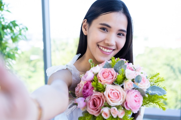 Valentinstag-Konzept, Selfie von Happy lächelnde asiatische junge Frau, die an einem Tisch sitzt und einen Rosenstrauß im Restauranthintergrund hält