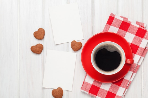 Valentinstag leere Bilderrahmen, Kaffeetasse und herzförmige Kekse über weißem Holztisch