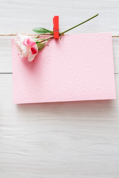 Valentinstag, leere Grußkarte und Rosenblume auf Wäscheklammer auf weißen rustikalen Holzbrettern
