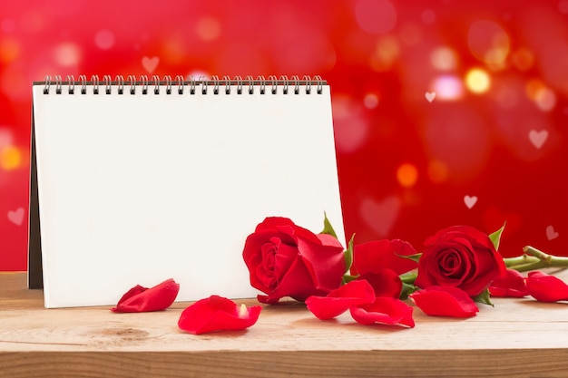 Valentinstag leeres Notizbuch mit roten Rosen und Blütenblättern auf Holztisch.