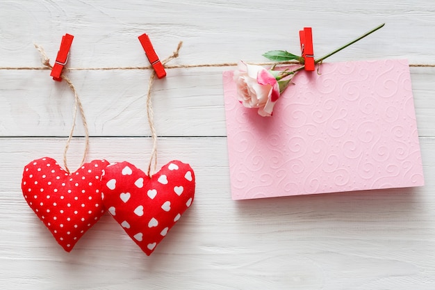 Valentinstag mit genähten Kissen diy handgemachte Herzen und leere Grußkarte auf roten Wäscheklammern an rustikalen weißen Holzbrettern