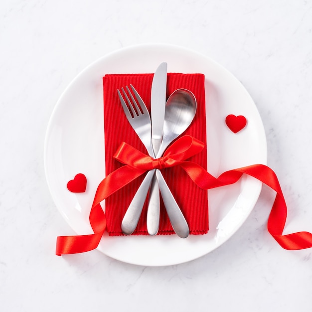 Valentinstag, Muttertag, Feiertags-Dating-Mahlzeit, Bankett-Design-Konzept - weiße Platte und rotes Band auf Marmorhintergrund, Draufsicht, flache Lage.