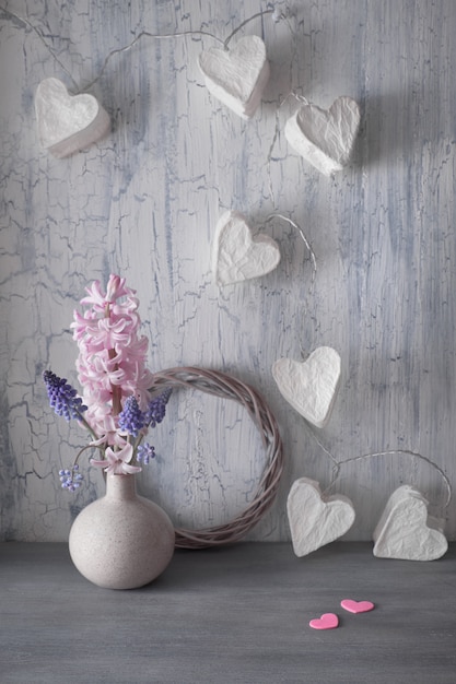 Valentinstag- oder Frühjahrfeier, Vase mit Hyazinthenblumen und Girlandenlichter mit Papierherzen