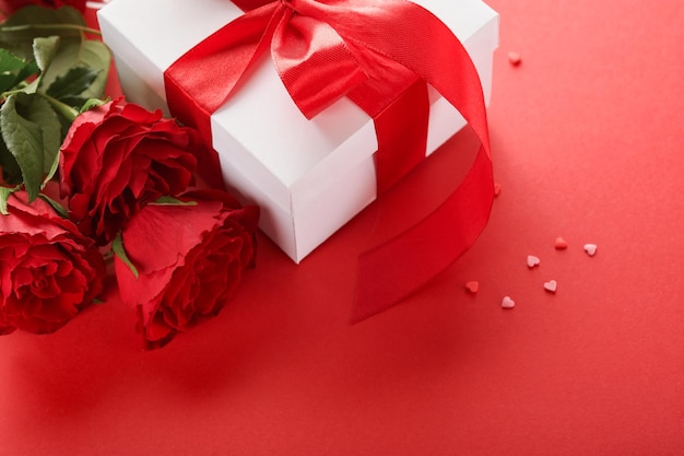 Valentinstag oder romantisches Abendessen Konzept Romantische Tischdekoration Besteck Weingläser Geschenkbox Rosen und Symbol der Liebe rotes Herz auf rotem Hintergrund Romantisches Abendessen Valentinstag Konzept