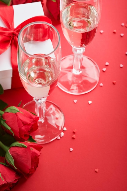 Valentinstag oder romantisches Abendessen Konzept Romantische Tischdekoration Besteck Weingläser Geschenkbox Rosen und Symbol der Liebe rotes Herz auf rotem Hintergrund Romantisches Abendessen Valentinstag Konzept