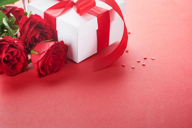 Valentinstag oder romantisches Abendessen Konzept Romantische Tischdekoration Besteck Weingläser Geschenkbox Rosen und Symbol der Liebe rotes Herz auf rotem Hintergrund Romantisches Abendessen Valentinstag Konzept