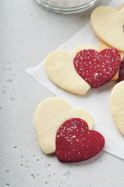 Valentinstag-Plätzchen Shortbread-Kekse in süßen roten Herzen mit Schokoladenglasur auf rosa Platte auf grauem Hintergrund Muttertag Frauentag Süße Feiertage Backen Valentinstagskarte Ansicht von oben