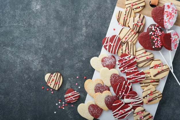 Valentinstag-Plätzchen Shortbread-Kekse in süßen roten Herzen mit Schokoladenglasur auf rosa Platte auf grauem Hintergrund Muttertag Frauentag Süße Feiertage Backen Valentinstagskarte Ansicht von oben