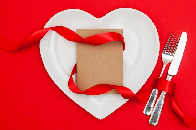Valentinstag-Speisekonzept Herzförmige Platte mit einer leeren Karte