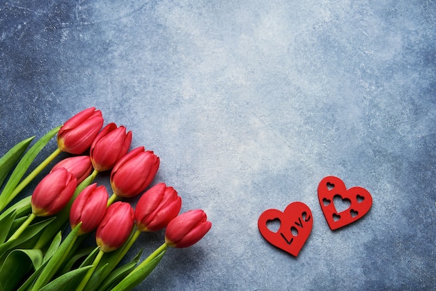 Valentinstag . Strauß roter Tulpen und zweier roter Herzen an einer blauen Wand. Flach liegen. Speicherplatz kopieren