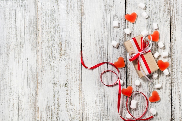 Valentinstag Süßigkeiten Herzen Marshmallows und Schachtel mit Geschenken in Bastelpapier über weißem Holzhintergrund.