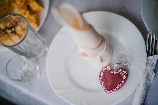 Valentinstag tischdekoration, flache rote schokoladenbonbons mit herzform auf weißem teller, gabel, messer und serviette auf festlichem tisch. valentinstag, liebe, dating-konzept, kopierraum. ansicht von oben.