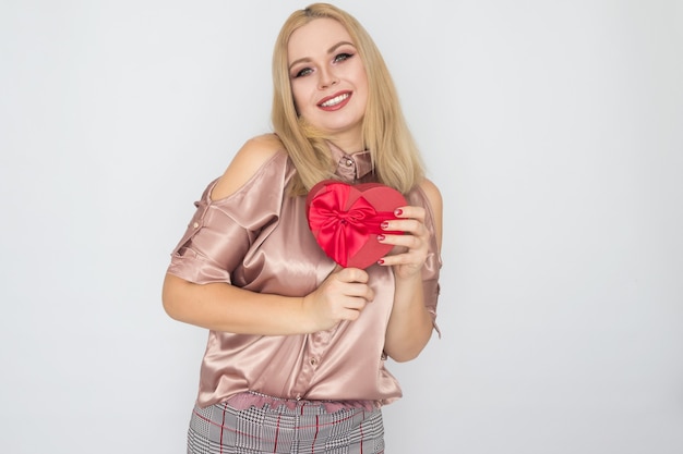 Valentinstag - träumende Frau in der rosa Bluse, die rotes Geschenkboxherz hält