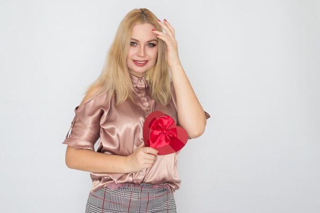 Valentinstag - träumende Frau in der rosa Bluse, die rotes Geschenkboxherz hält