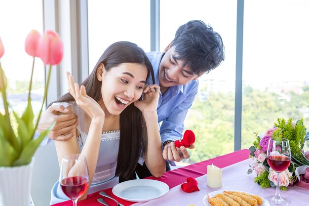 Valentinstag und asiatisches junges glückliches süßes paarkonzept, asiatischer mann mit verlobungsring, der der frau nach dem mittagessen einen heiratsantrag macht in einem restauranthintergrund, hochzeitspläne für braut und bräutigam