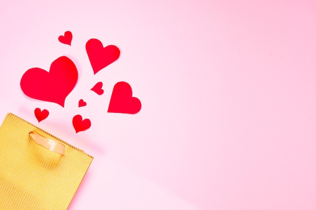 Valentinstag Wohnung lag Kopierraum. Goldene Papiergeschenktüte und rote Herzen auf rosa Papierhintergrund.