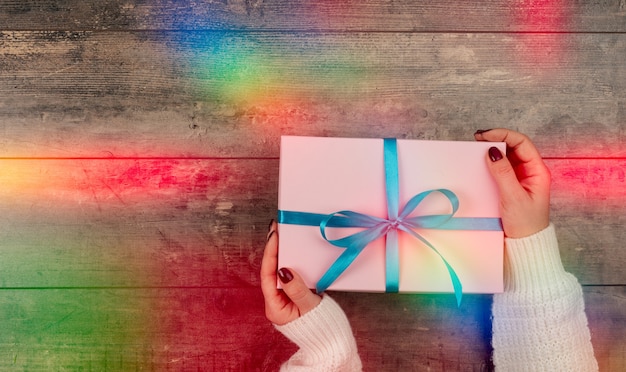 ValentinstagFrau, die Geschenkbox mit roter Schleife über Feiertagshintergrund hältweibliche Hände, die Geschenk halten