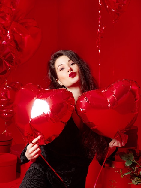 Valentinstagfrau in Schwarz mit roten herzförmigen Luftballons, die Spaß haben