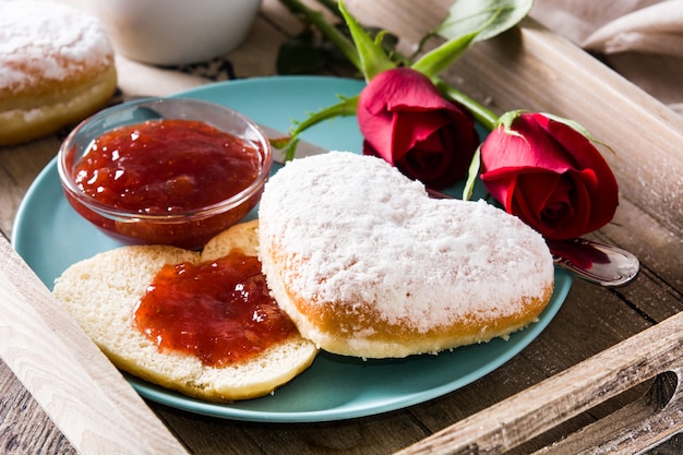 Valentinstagfrühstück mit Kaffee, herzförmigem Brötchen, Beerenmarmelade und Rosen auf einem Tablett