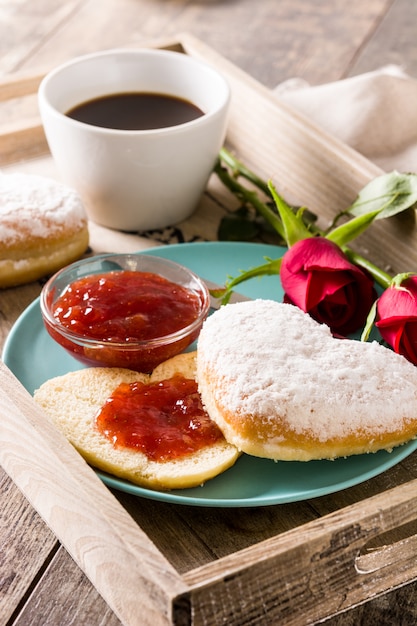 Valentinstagfrühstück mit Kaffee, herzförmigem Brötchen, Beerenmarmelade und Rosen auf einem Tablett
