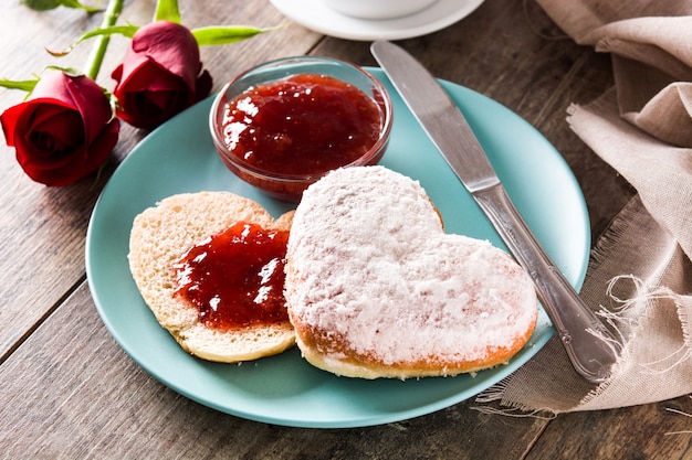 Valentinstagfrühstück mit Kaffee, herzförmigem Brötchen, Beerenmarmelade und Rosen