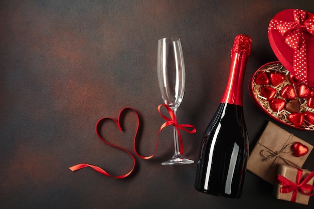 Valentinstaggrußkarte mit Champagnergläsern und Liebesgeschenkbox auf Steinhintergrund.