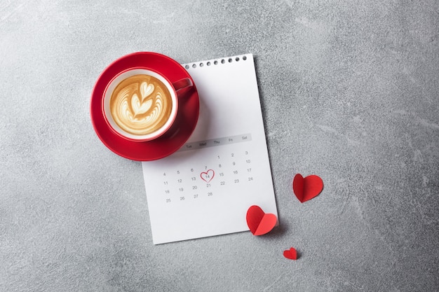 Valentinstaggrußkarte. Rote Kaffeetasse und Geschenkbox über Februar-Kalender. Ansicht von oben