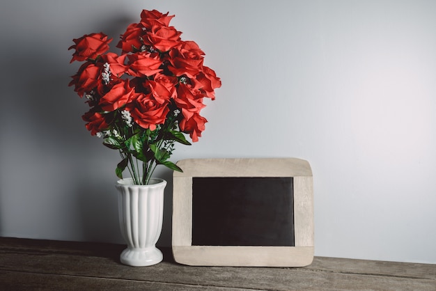 Valentinstaggrußkarte. Rotrosenblumen und -tafel auf Holztisch.