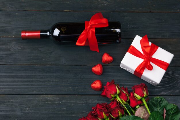 Valentinstaggrußkarte, Rotrosenblumen, Wein und Geschenkbox auf Holztisch.