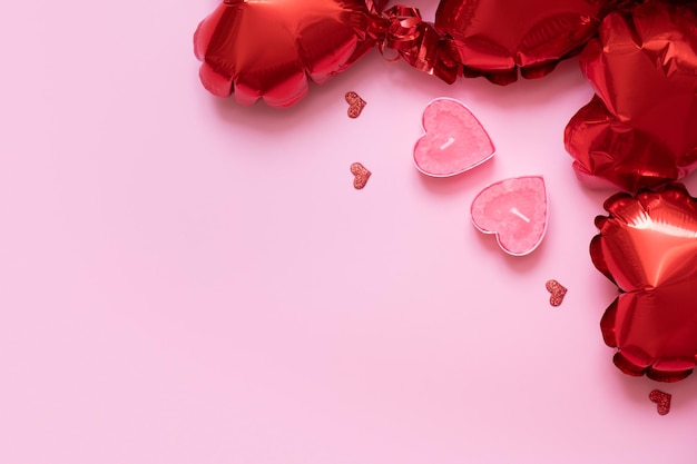Valentinstaghintergrund mit Kopienraum und zwei Kerzen mit roten Herzformballonen auf rosa Hintergrund