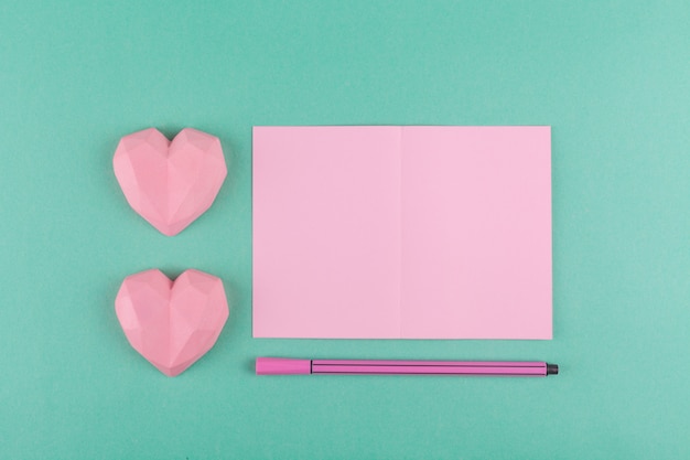 Foto valentinstagkonzept, minimalismus. rosa grußkarte, stift, herz auf einem papierhintergrund der grünen minze.