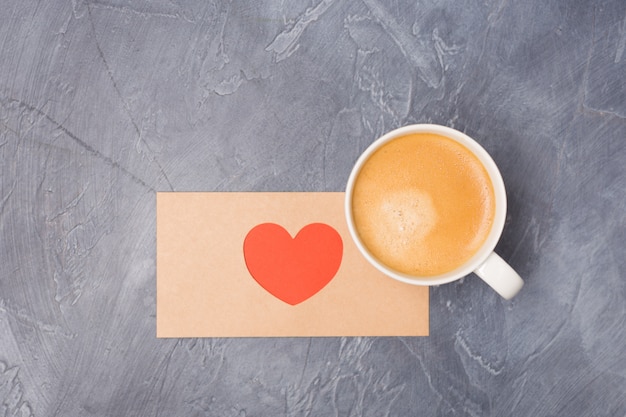 Valentinstagliebesbrief und -kaffee auf grauem Schreibtisch. Fertigkeit schlagen mit rotem rotem Herzen und freiem Raum des Kaffees ein