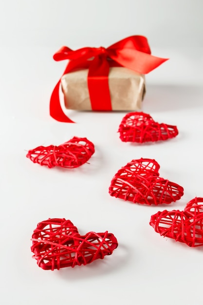 Valentinstagsgeschenk und rote Herzen auf einem weißen Hintergrund. Valentinstaggeschenk auf einem Hintergrund der roten Herzen von Zweigen der Zweige, vertikales Foto